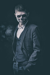 Fototapeta na wymiar Stylish and beautiful, emotional young man with skeleton makeup in a strict suit against the background of smoke and dark background to Halloween