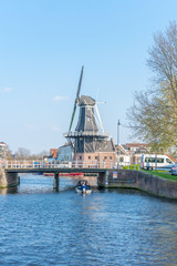 Fototapeta na wymiar Haarlem, Netherlands – April 14, 2019: View of Harlem Cityscape With De Adriaan Windmill on Spaarne River On Background At Noon in Haarlem, The Netherlands