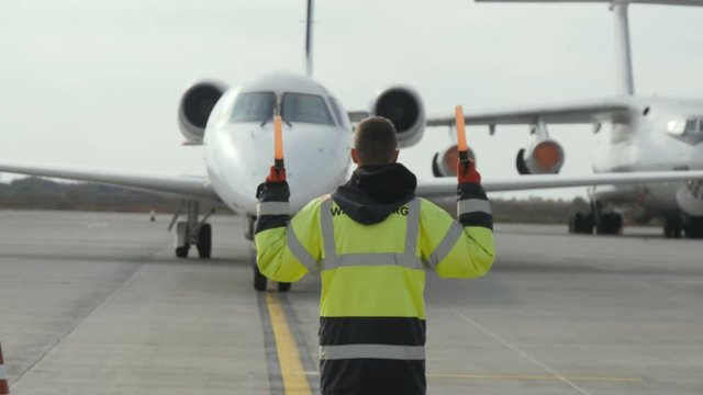 Aerodrome employee in uniform regulating moving big airplane in airport 