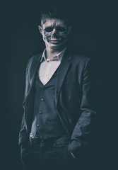 Stylish and beautiful, emotional young man with skeleton makeup in a strict suit against the background of smoke and dark background to Halloween