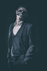 Stylish and beautiful, emotional young man with skeleton makeup in a strict suit against the background of smoke and dark background to Halloween