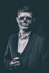 Stylish and beautiful, emotional young man with skeleton makeup in a strict suit against the background of smoke and dark background to Halloween