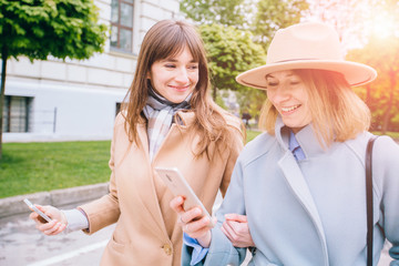 Two adult women sisters bloggers friends walking stylish people best students travelers use apps news gesture stroll show adverts recommend advise look choose sale specs spring outfit town square.