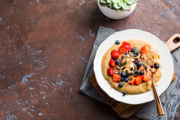 Gluten free amaranth topped with homemade almond butter, fresh strawberries, sesame, pumpkin seeds. Vegan plant based breakfast served on dark wooden board. Healthy colorful food concept.
