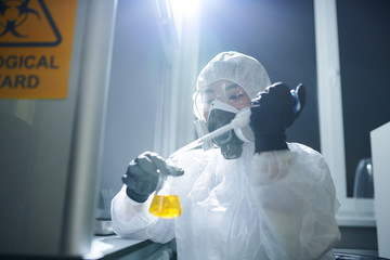 Concentrated microbiologist wearing protective goggles, biohazard suit and respiratory mask...