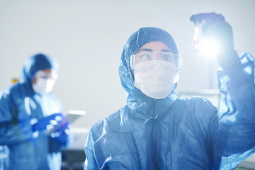 Serious pensive Asian virologist in blue biohazard suit and safety goggles standing in scientific...