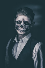 Stylish and beautiful, emotional young man with skeleton makeup in a strict suit against the background of smoke and dark background to Halloween