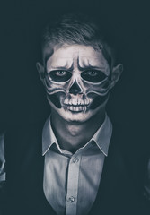 Stylish and beautiful, emotional young man with skeleton makeup in a strict suit against the background of smoke and dark background to Halloween