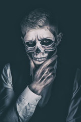 Stylish and beautiful, emotional young man with skeleton makeup in a strict suit against the background of smoke and dark background to Halloween