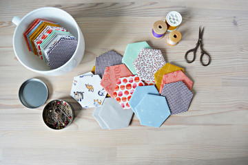 Hexagon english paper piecing templates, white cup, thread, retro scissors and metal pins on the wooden table