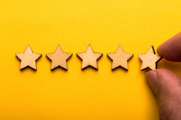Hand putting wooden five star shape on yellow background