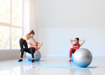 Fototapeta premium Young sporty women with fitballs doing exercises under supervision of trainer in gym