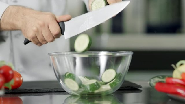Chef cutting fresh cucumber in glass bowl in slow motion at kitchen