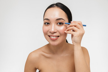 Beautiful young pretty asian woman with healthy skin posing naked isolated over white wall background holding eye pencil.