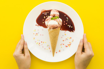 Person holding plate with ice cream in waffle cone