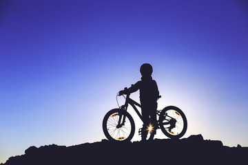Silhouette of a little girl with a bicycle at sunset