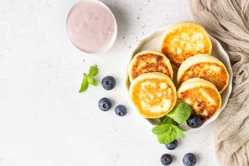 Cottage cheese fritters (syrniki) with fresh blueberries, mint and sauce. Light grey background. Healthy breakfast or diet lunch. Copy space.