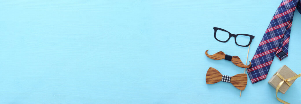 Father's day concept. Hipster glasses, goft box tie and funny moustache over blue wooden background. top view, flat lay