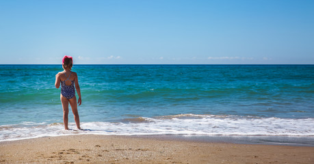The girl stands with her back on the beach against the backdrop of a beautiful wave