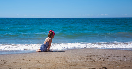 The girl seats with her back on the beach against the backdrop of a beautiful wave