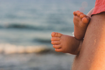 Baby feet in father's hands. Dad holding sleeping baby, outdoor sea portrait. Family and bonding concept