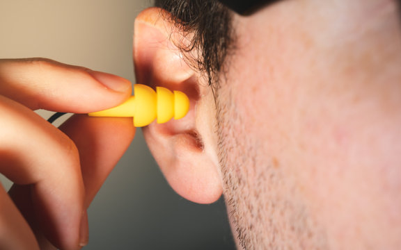 Man worker inserting yellow hearing safety protection earplug in his ear close up view