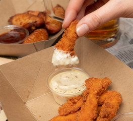Mano mojando pollo frito en salsa blanca sobre mesa