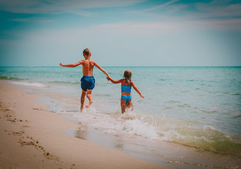 happy girl and boy run play with waves on beach