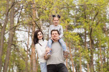 Happy family: mother, father and little daughter outdoor. Parents giving child