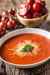 Hot tomato soup parmesan cheese and basil leave on old oal table