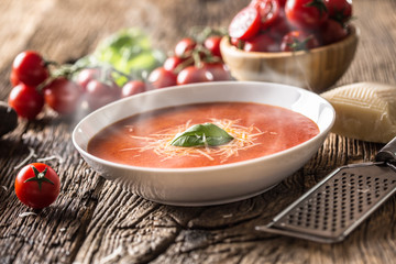 Hot tomato soup parmesan cheese and basil leave on old oal table