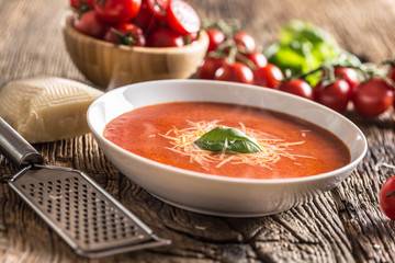Hot tomato soup parmesan cheese and basil leave on old oal table