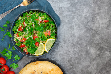 Tabbouleh salad with bulgur, parsley, spring onion and tomato in bowl on grey background. Top view. WIth copy space