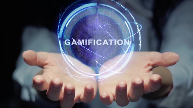 Female hands show a round conceptual hologram with text Gamification. Unrecognizable woman in ashen white on a black background with future holographic technology