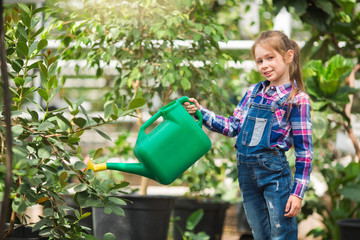 beautiful young girl watering a watering-can tree with lemons in a greenhouse garden