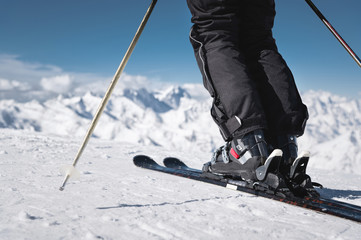 Close-up of the athlete's skier's foot in ski boots rises into the skis against the background of the snow-capped Caucasus mountains on a sunny day. Winter sports concept - obrazy, fototapety, plakaty