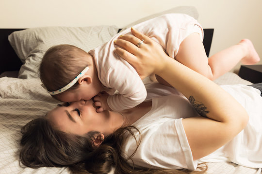 Young mother and baby are in bed. Mom and baby are playing at home. Authentic lifestyle photos.