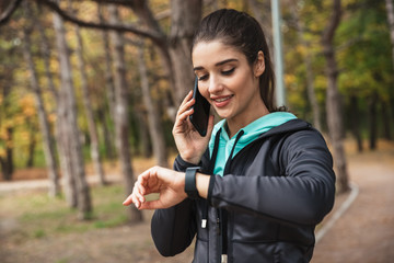Pretty fitness woman outdoors in the park looking at watch clock.