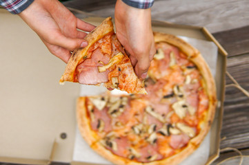 Boy hand holding a slice of delicous pizza, eating pizza in a park