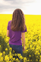 Fototapeta premium Young girl on a background of yellow field flowers. Beautiful stylish romantic. Colza, rapeseed, canola.
