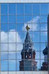 Reflection of the Christian Orthodox Church in mirrored glass on the modern building of the shopping center. Old Church with Golden domes, crosses and bell tower.