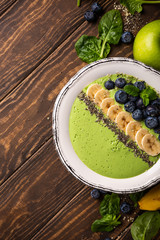 Breakfast detox green smoothie bowl from banana and spinach on wooden background. Healthy food concept with copy space, top view