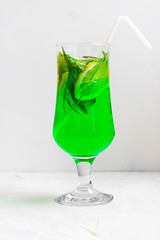 Summer cold green drink made from tarragon, with mint and slices lemon in glass with straw on light background. Sparkling beverage, lemonade. Horizontal with copy space