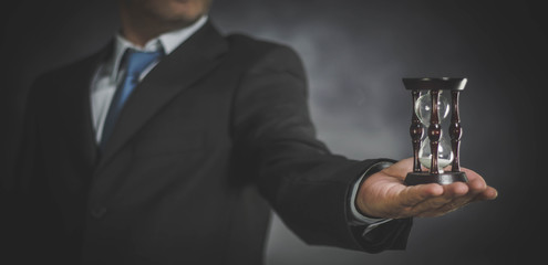 businessman holding hourglass in hand on dark background