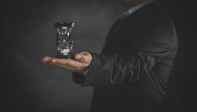 businessman holding hourglass in hand on dark background