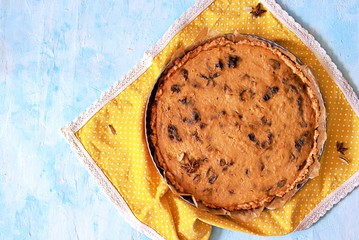 Whole pumpkin pie with prunes in a baking dish on a light blue background