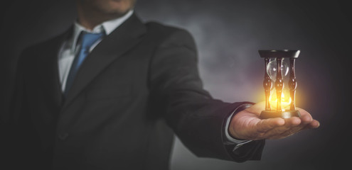 businessman holding hourglass in hand on dark background