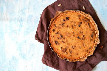 Whole pumpkin pie with prunes in a baking dish on a light blue background