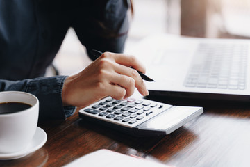 Woman entrepreneur using a calculator to calculating financial expense at coffee shop.