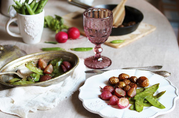 young summer vegetables-fried radish, young peas and young potatoes. dinner served at the table, beautiful table setting.